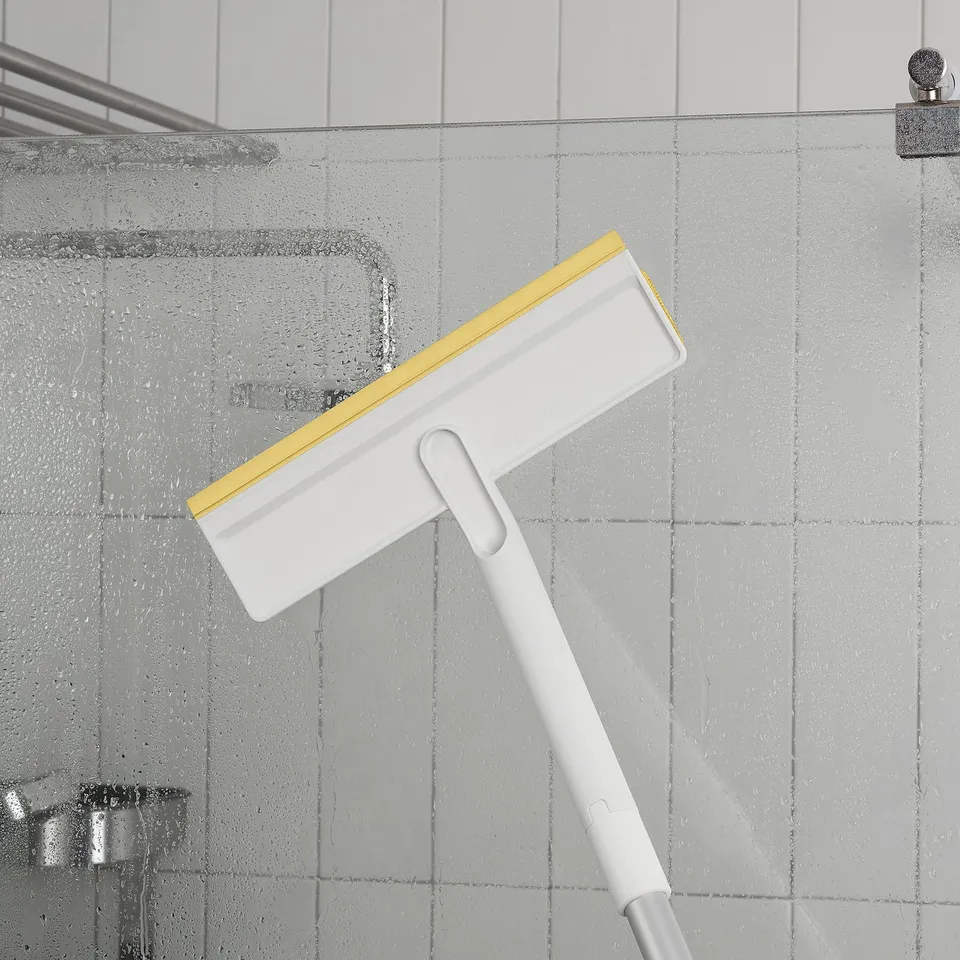 White PEPPRIG squeegee with yellow blade cleaning shower glass door.