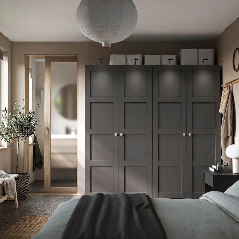 Modern bedroom with black PAX wardrobe, grey handles, and top storage. Cosy bed with blue blanket, lantern light, and green plant.