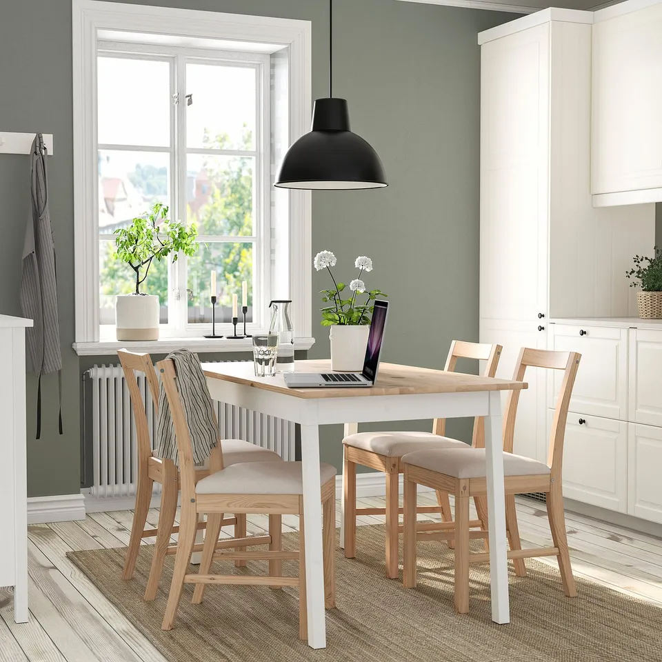 Modern PINNTORP dining setup with white table, light wood chairs, laptop, decor, and pendant light.