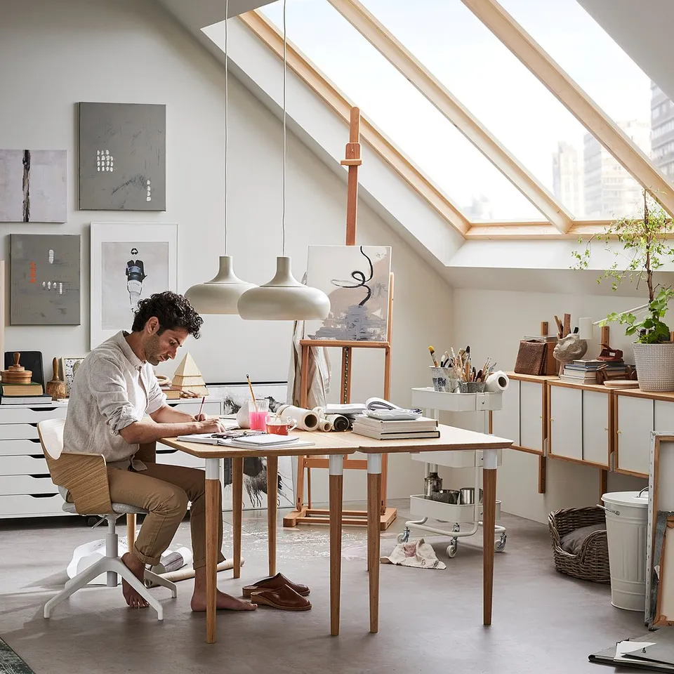 Person drawing at bamboo desk in bright, modern room with natural light.