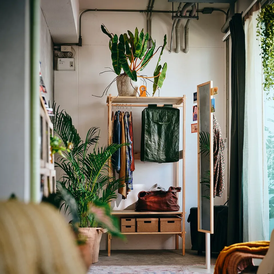 KRONÖREN wood shelf. Natural finish, with hanging rail. Clothes and plants nearby.
