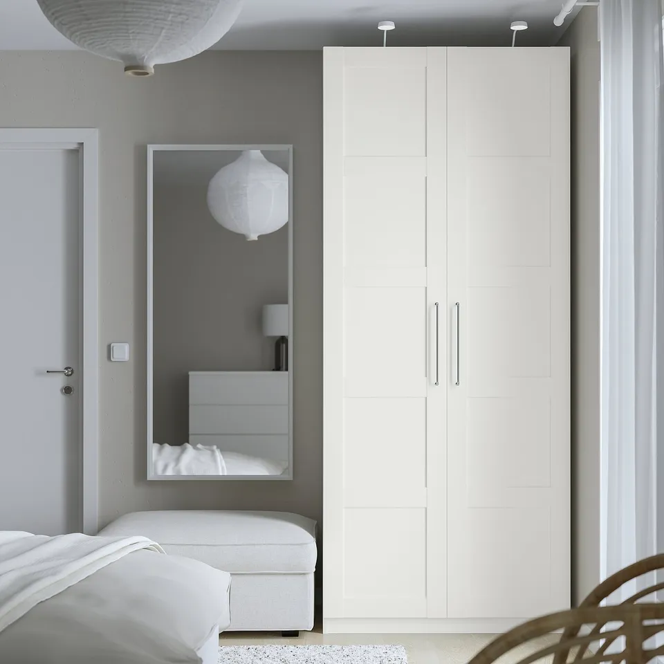 Minimalist bedroom with large PAX closet, mirror, bed, white bench, and pendant lights.