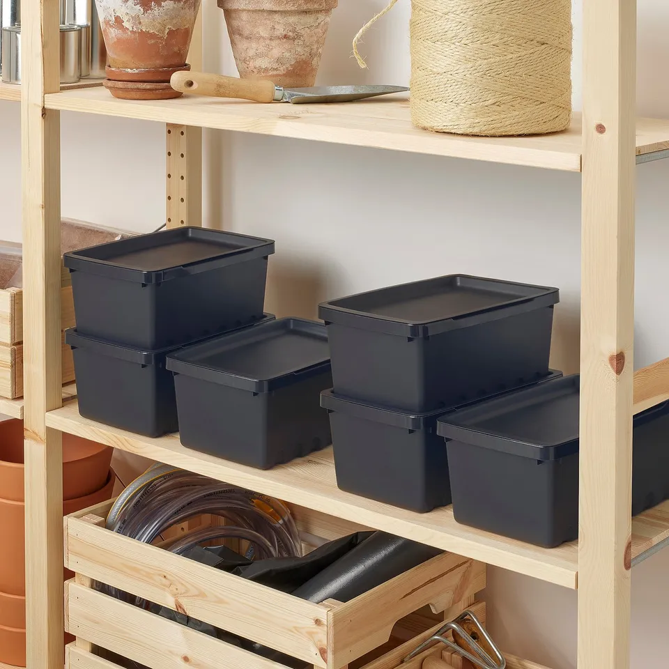 Shelf with stacked, lidded plastic boxes for storage, on top of wooden shelves with clay pots and gardening tools.