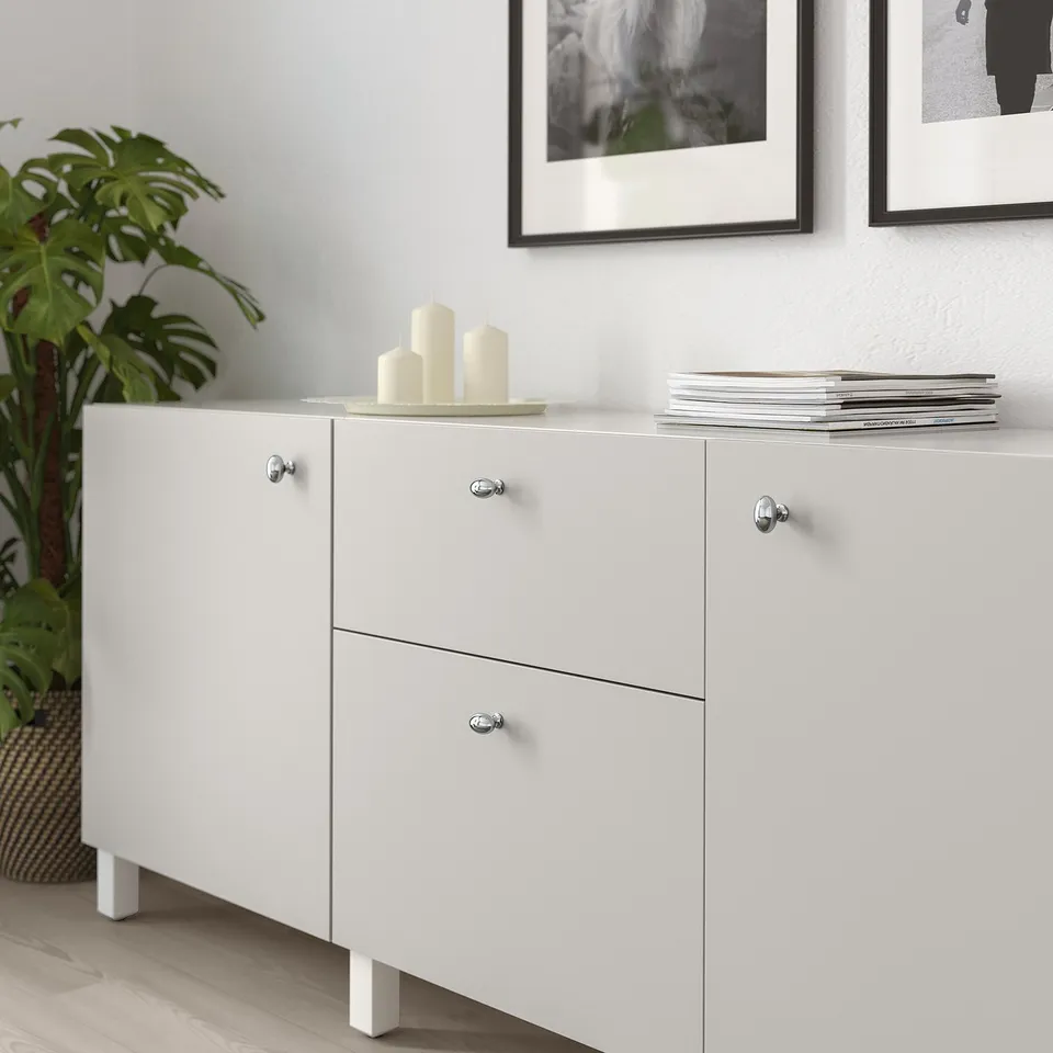 White cabinet with knobs; candles and plant on top; framed art behind.