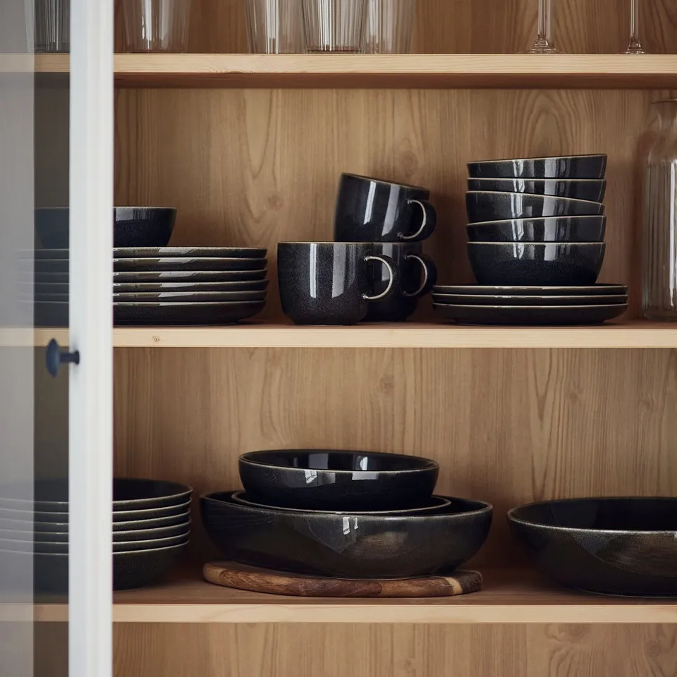 Shelf with GLADELIG stoneware plates, mugs, and bowls in dark grey.