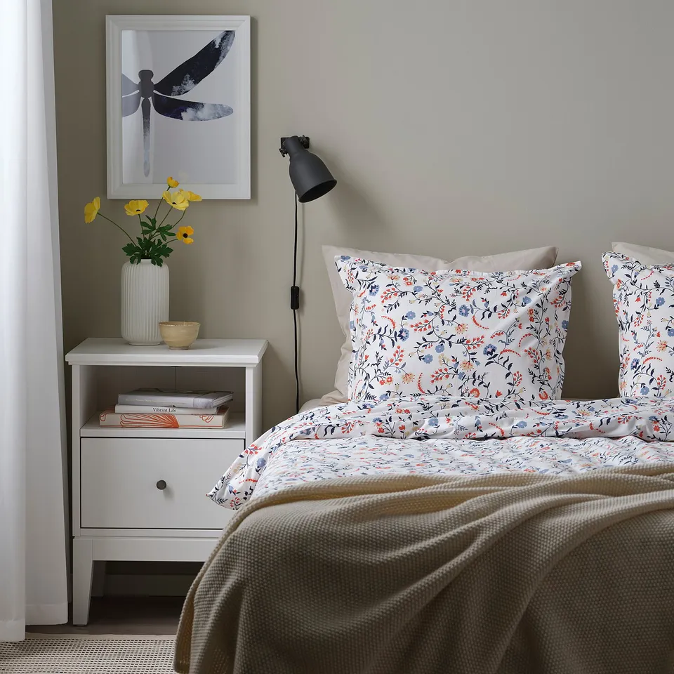 Cosy bed with BRUDKRUSBÄR duvet, bedside table, lamp, and yellow flowers.