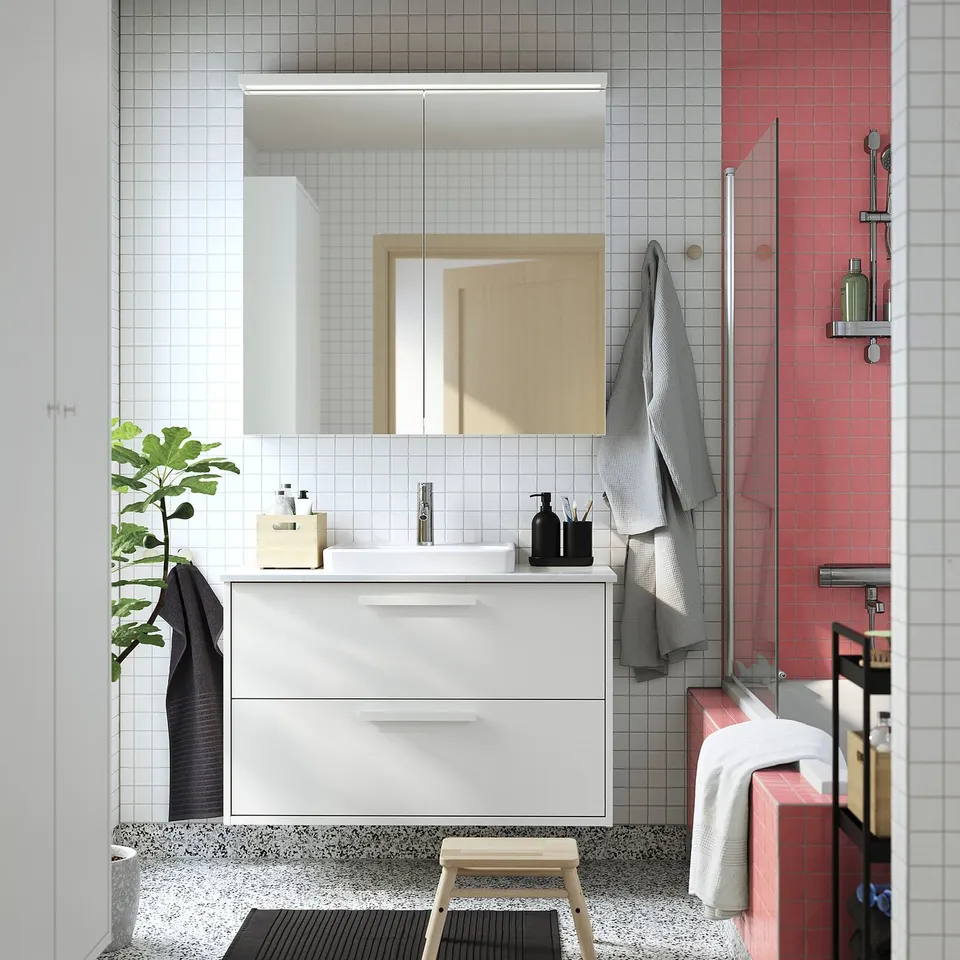 Modern bathroom with white ikea TOLKEN countertop, plant, towels, and red-tiled shower.