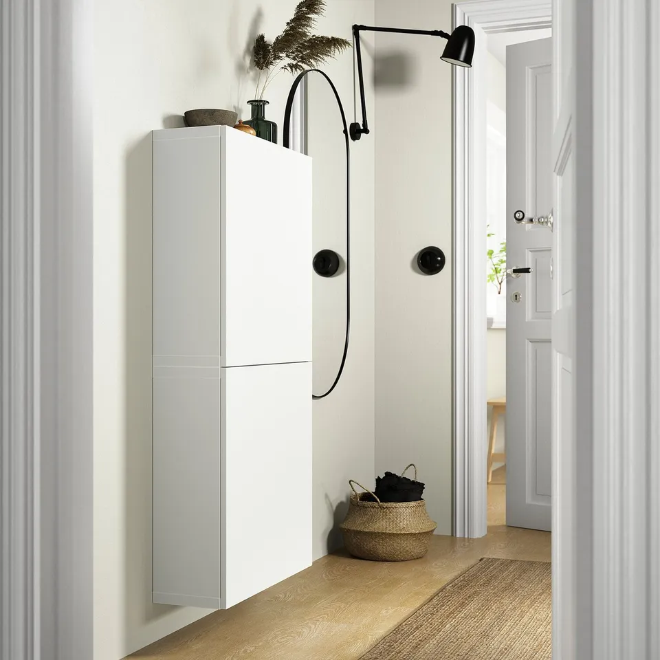 White BESTÅ storage unit with black accents and light wood floor in entryway.