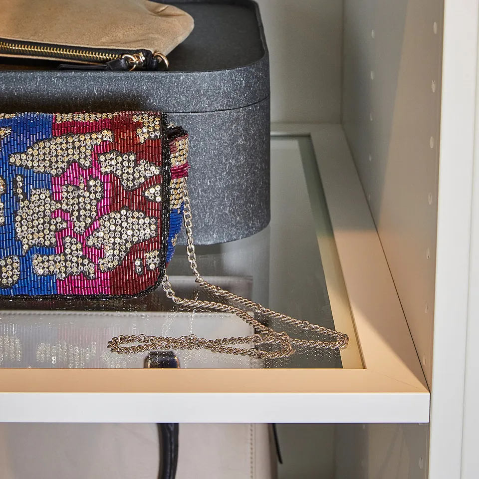 A glass shelf in a wardrobe holds colourful, beaded purses; one with pink and blue hues hangs over the edge.