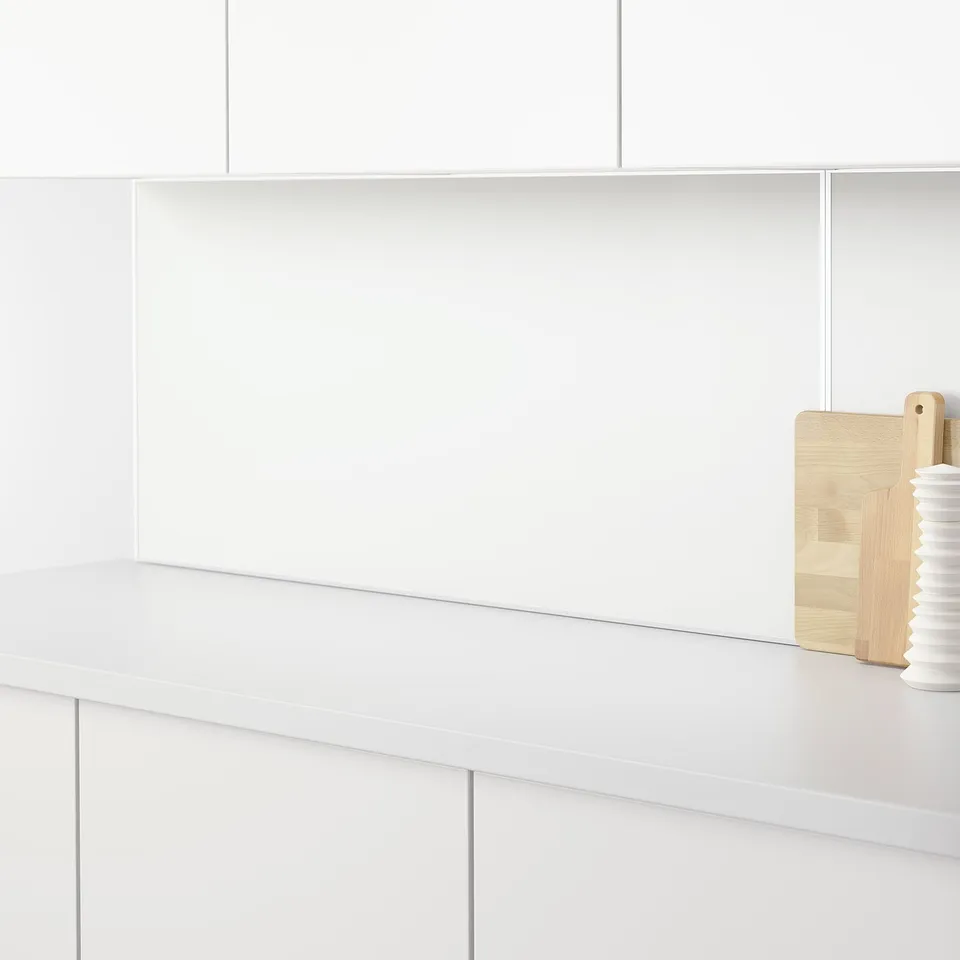 White kitchen counter with cutting boards and ceramic item. LYSEKIL panels protect walls.