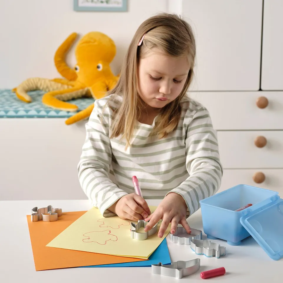 Young girl uses cookie cutters to trace shapes on coloured paper, developing motor skills.