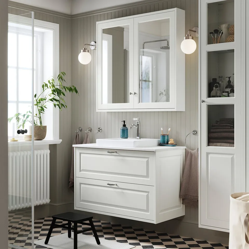 Modern bathroom with TÄNNFORSEN white cabinet, mirrored doors, sink, and black floor tiles. Plant and stool added.
