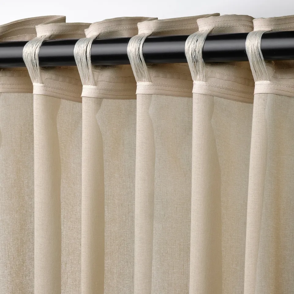 Beige sheer curtains hang on black rod, filtering light, offering privacy. Hooked with tabs, they create soft pleats.
