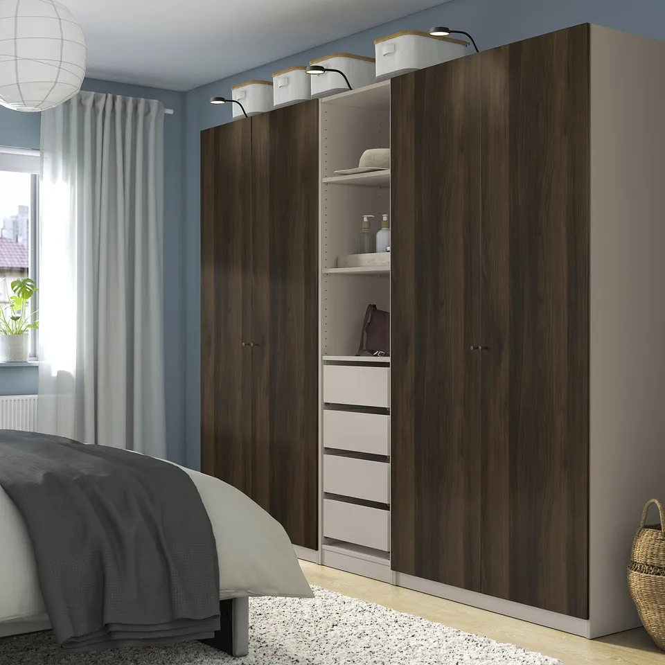 Modern bedroom with large wood PAX wardrobe, light grey walls, dark bedding. Wardrobe is tall, rectangular, with multiple compartments.
