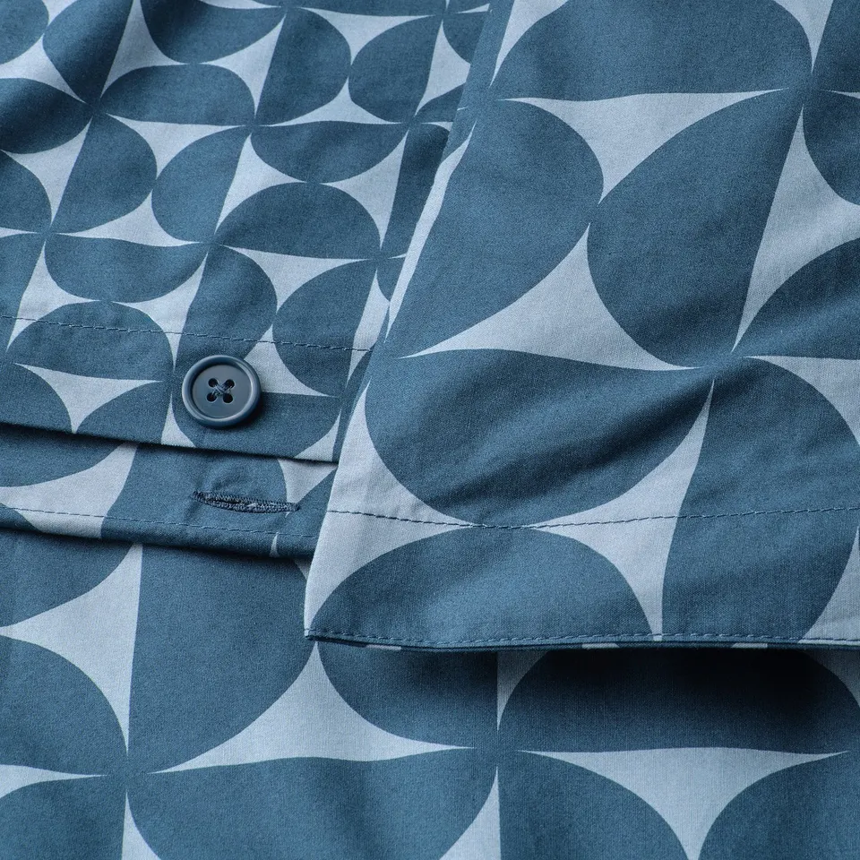 Close-up of a fabric with a geometric pattern of interlocking shapes in dark and light blue. A button closure is visible at the cuff.