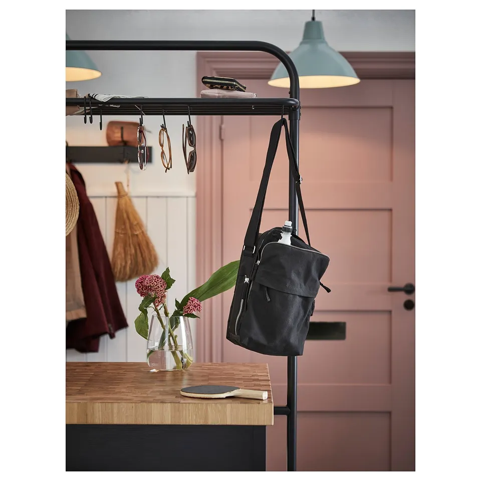 Black VADHOLMA kitchen rack with backpack, glasses, vase, flowers. Brown door, blue lamps, coats.