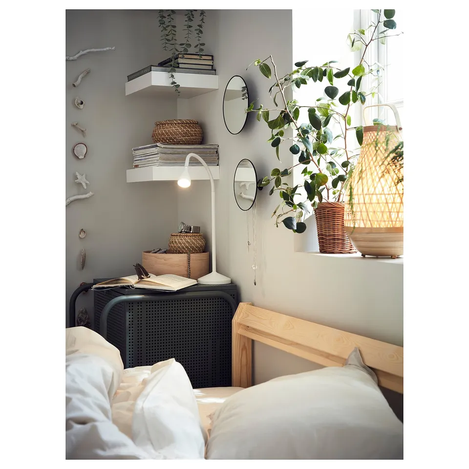 Cosy bedroom with white bedding, wooden headboard, books, plants, mirrors, and adjustable NÄVLINGE lamp.