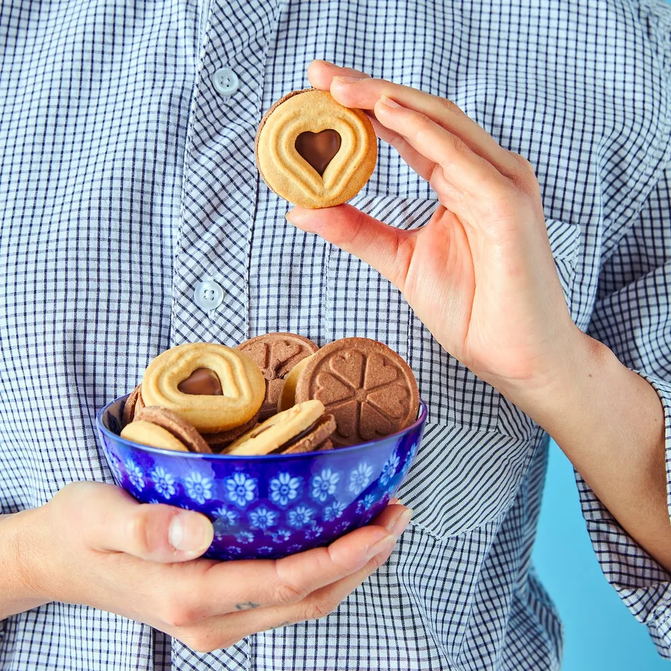 Person holding a blue bowl filled with heart-shaped cookies and a single heart-shaped cookie with a bite missing.