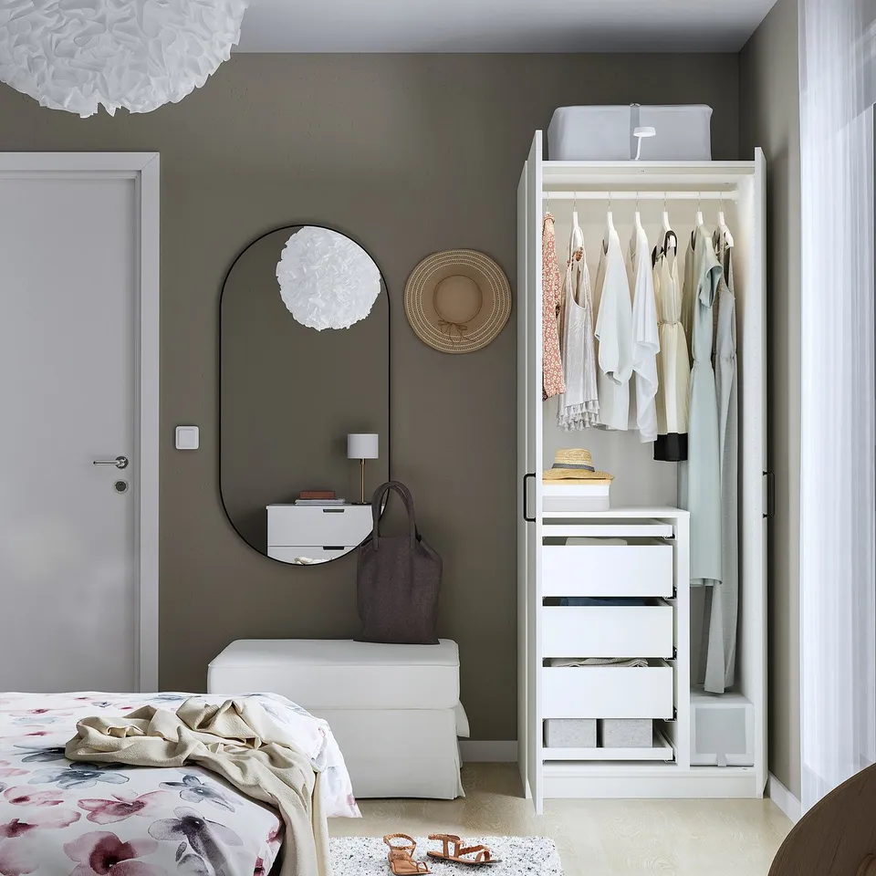 Minimalist bedroom with PAX wardrobe, pendant lamp, mirror, and bed with floral blanket.