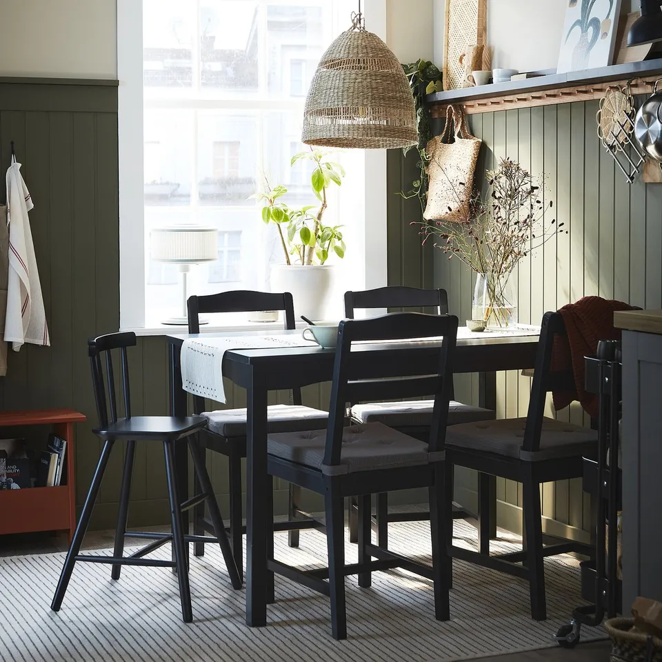 Cosy dining nook with HÄGERNÄS table, chairs, pendant light, window, plant, and striped rug.