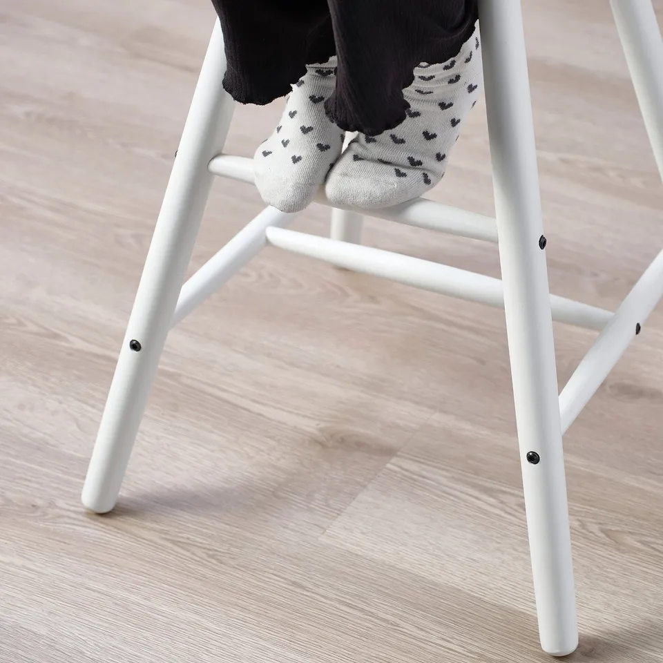 Child sitting on white junior chair with feet on wooden legs, wearing grey socks with black patterns.