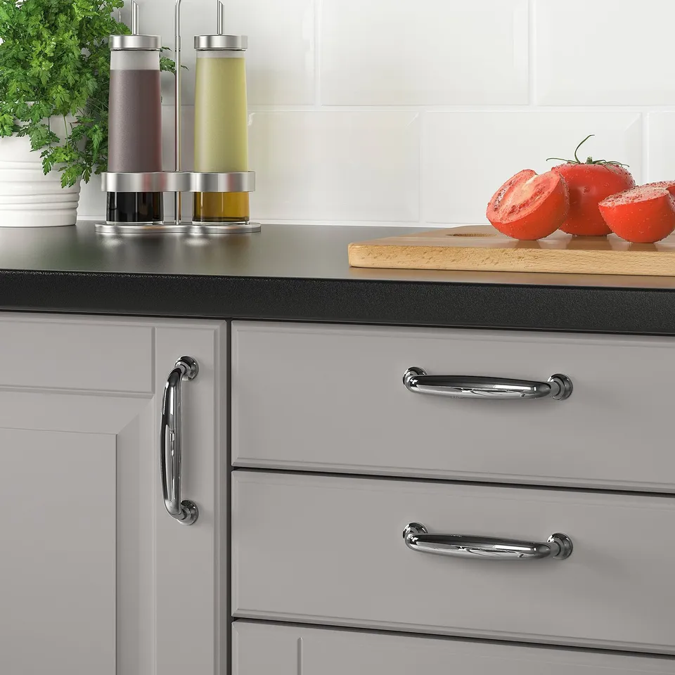 Modern kitchen cabinet with chrome handles, a wooden cutting board, sliced tomatoes, and seasoning dispensers on the countertop.