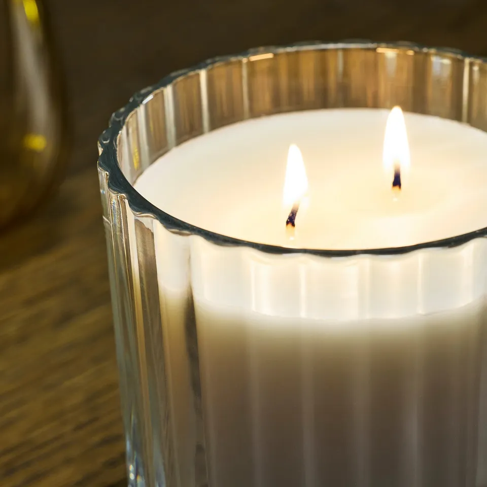 Lit three-wick candle in decorative glass, emitting soft light and gentle scent.