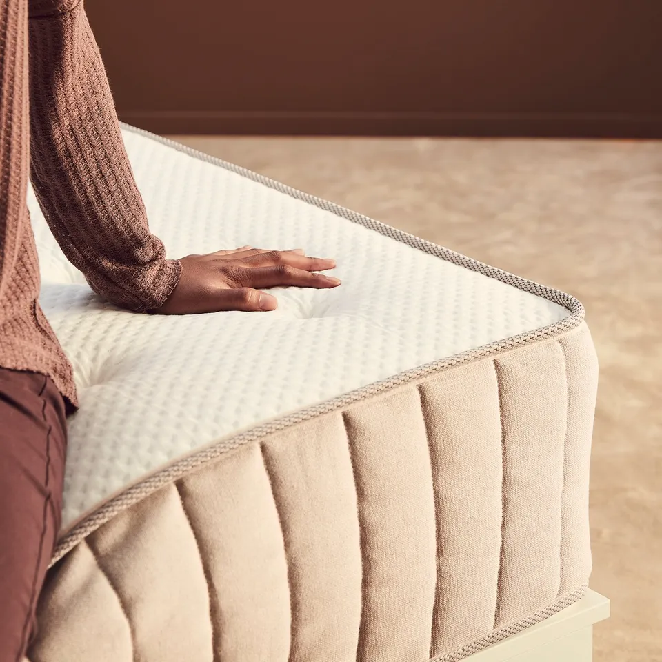 Person testing firm white mattress with natural materials.