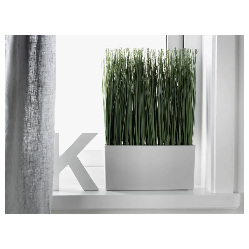 A modern white shelf holds a rectangular white planter with tall artificial grass and a geometric decor piece, ideal for indoor/outdoor use.