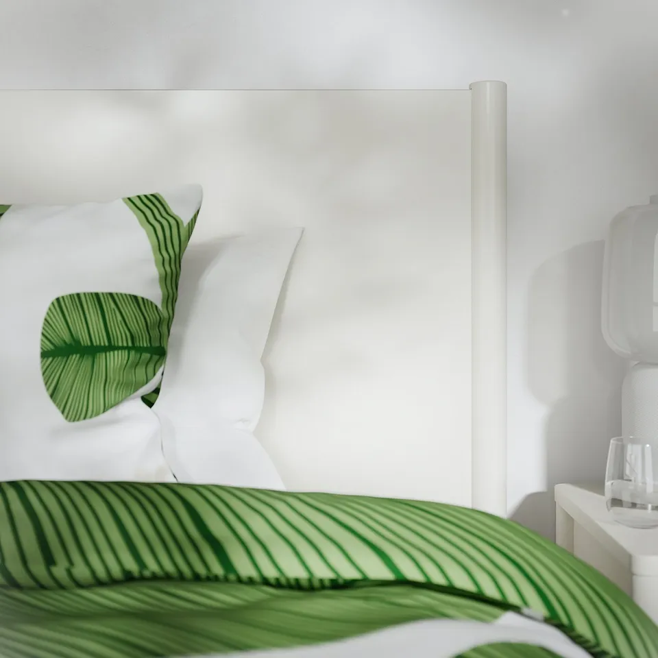 Modern white bed with leaf-patterned green pillows and blanket, showcasing quality design and soft-closing drawers.