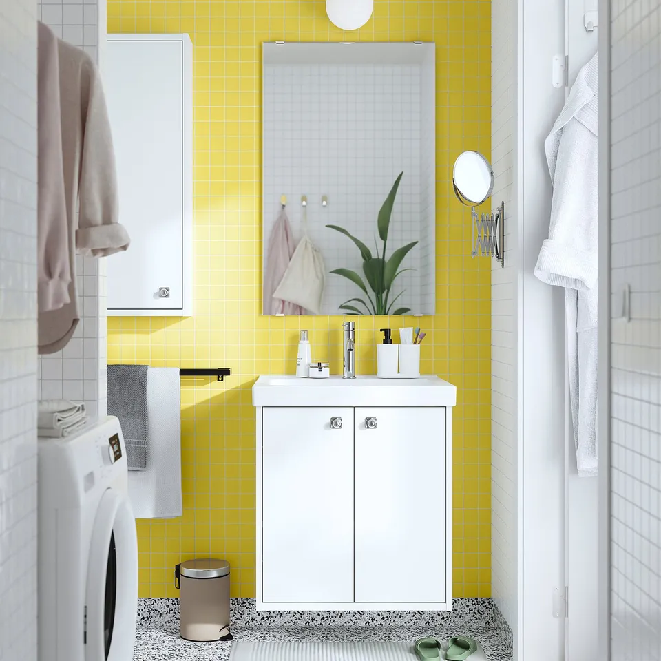 Bright yellow-tiled bathroom with white HAVBÄCK vanity, small, rectangular sink, mirror, and plant. Includes washing machine and hanging robes.