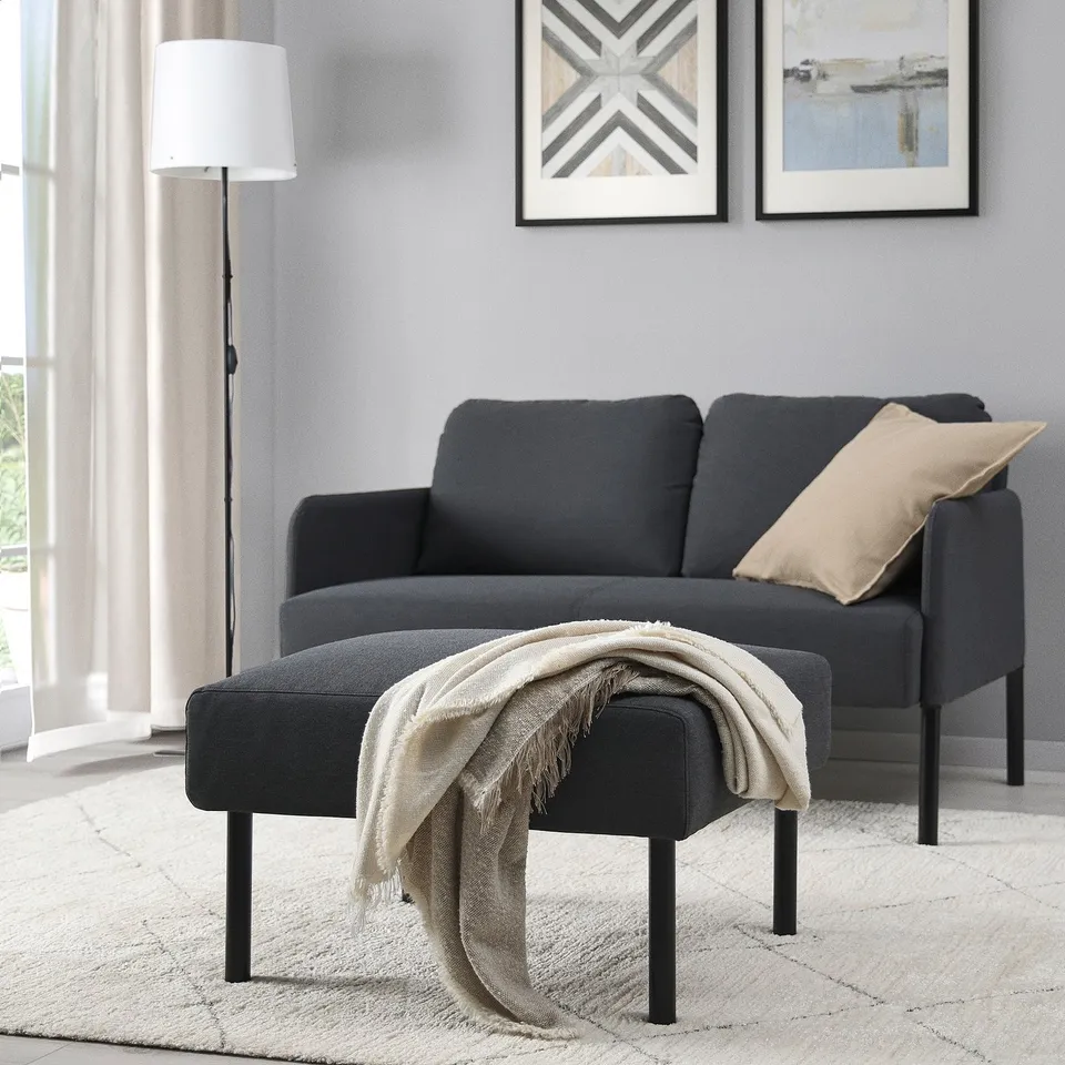 Modern living room with dark grey GLOSTAD sofa & matching footstool. Footstool is smaller, positioned in front. Decorated with beige throw & pillow.