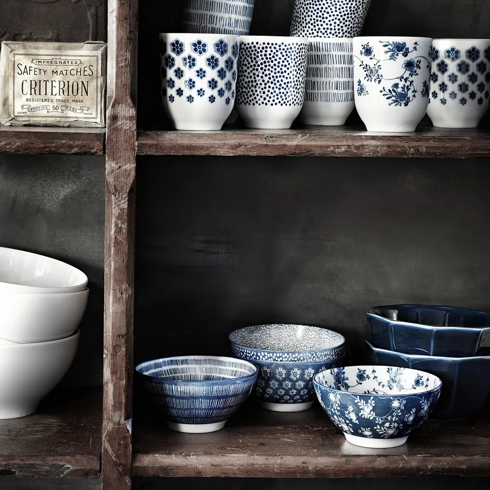 Shelf with blue and white patterned mugs and bowls; some plain white items; wooden shelf; old safety matches box.