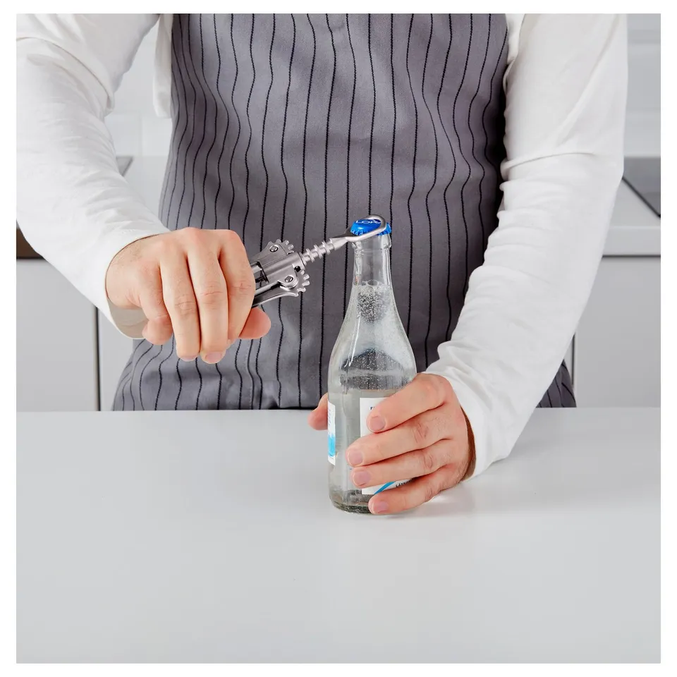 Person holding a bottle with a bottle opener on the handle, ready to open the bottle on a white surface.