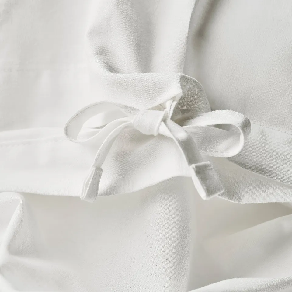 A close-up of white duvet covers bow detail, showcasing its lace trim and fabric tie closure.