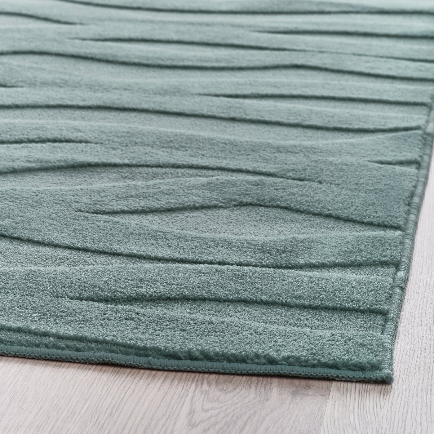 Soft, textured, blue rug with 3d wave pattern on a light wooden floor.