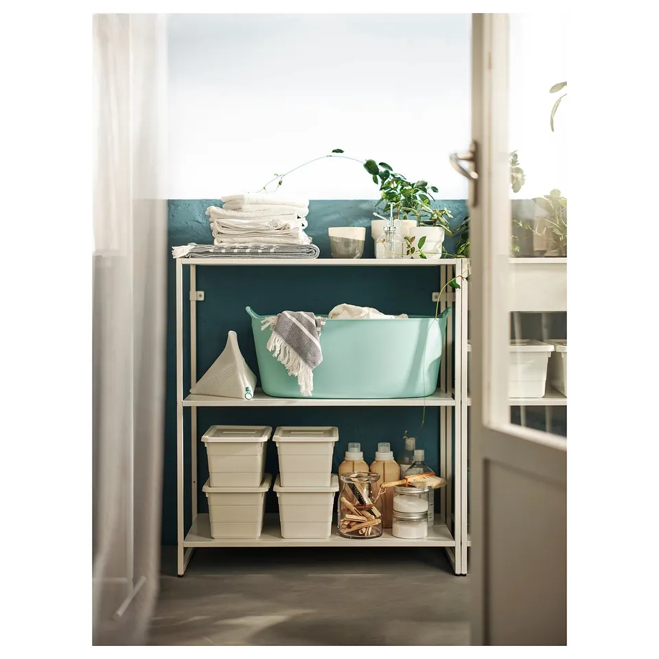 JOSTEIN white metal shelving unit with blue basket, towels, and cleaning supplies.