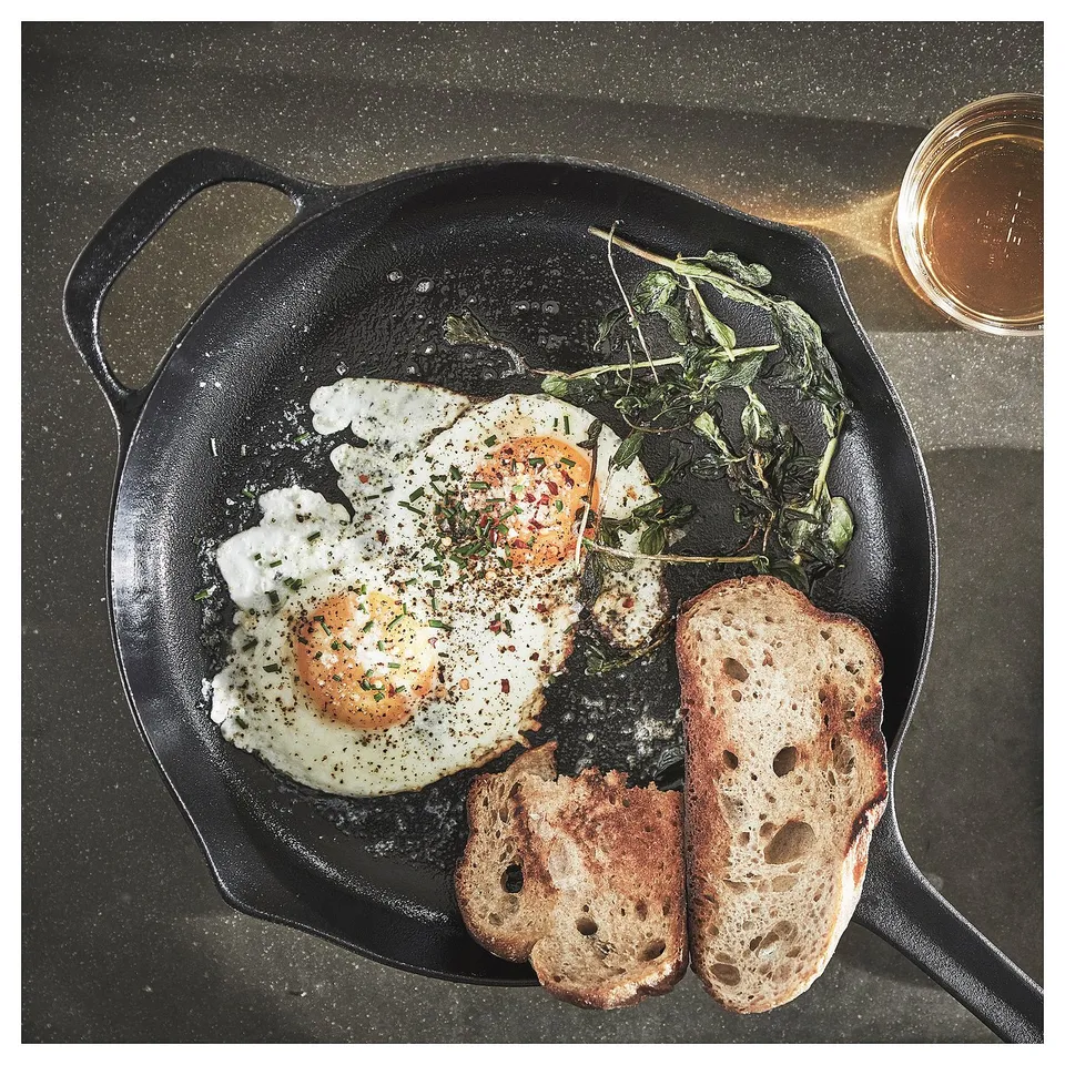 Black cast-iron skillet with fried egg, greens, and toast. Seasoned with herbs and spices.