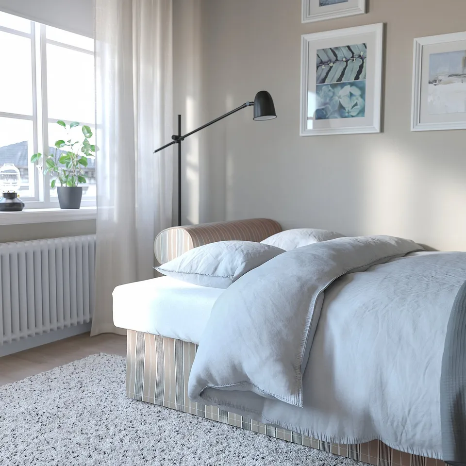 Modern bedroom with white bed, large window, floor lamp, potted plant, and framed art.
