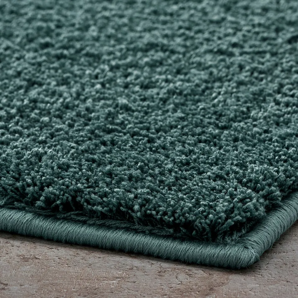 Thick, plush bath mat; soft, recycled polyester; secure latex backing; deep green hue.