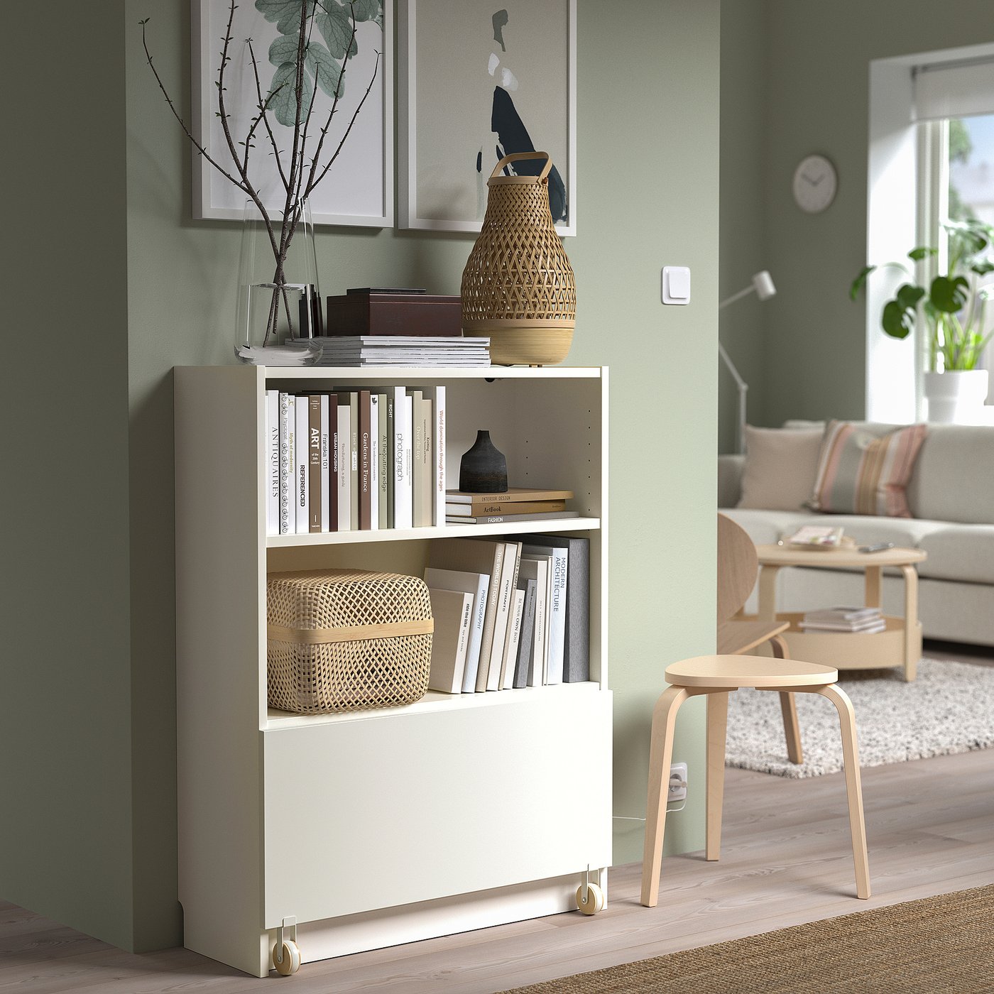 Living room with white BILLY bookcase, drawer, shelves, green walls, beige sofa, stool.