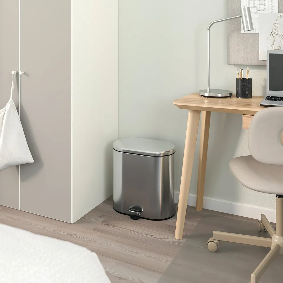 Sleek stainless steel STABBEN bin in modern office setting next to light wood desk with laptop and lamp.