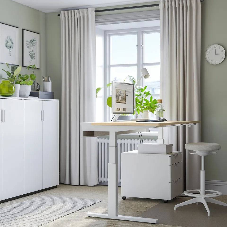Home office with MITTZON white sit/stand desk, chair, & storage. Large window & plants.
