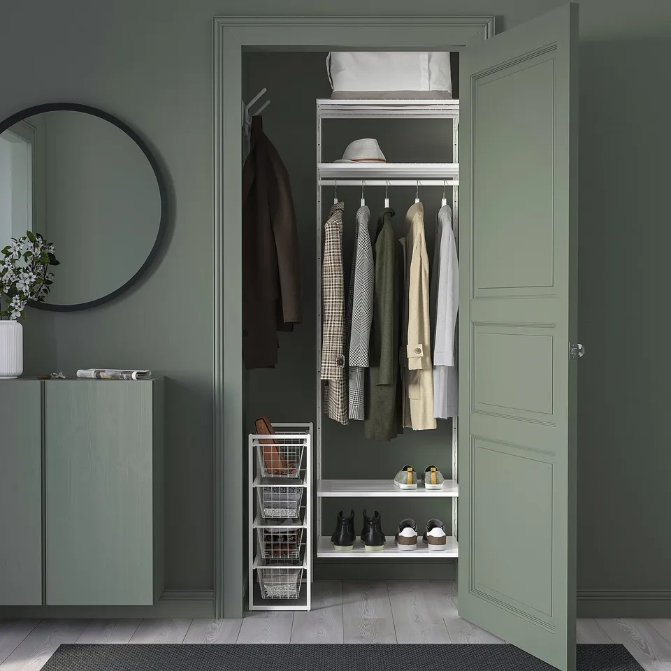 Small, white, wire JONAXEL storage basket sits neatly beneath clothes, fitting well in organised closet.