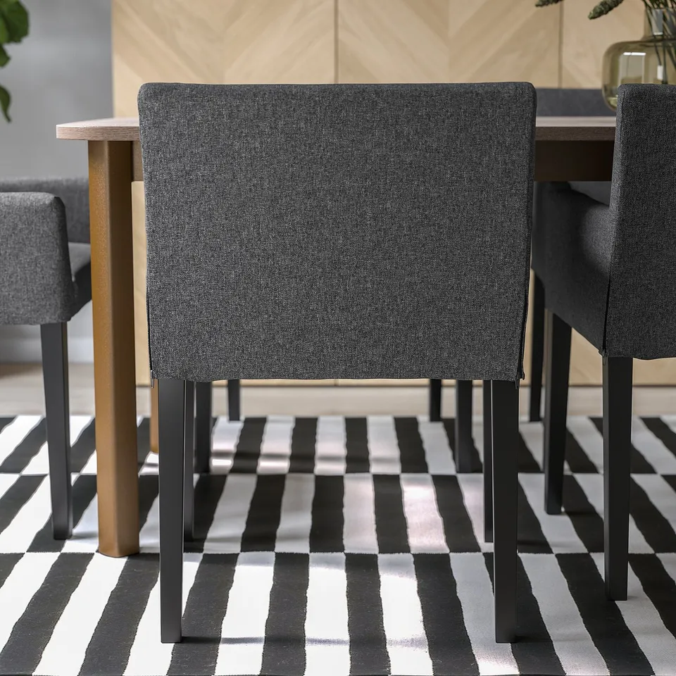 Two dark grey dining chairs with black metal legs and armrests on a black/white rug near light wood table.
