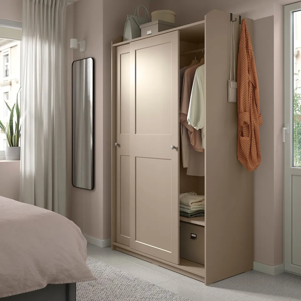 Bedroom with HAUGA beige wardrobe, open doors showing clothes and shelves. Mirror, bed, and orange towel feature.