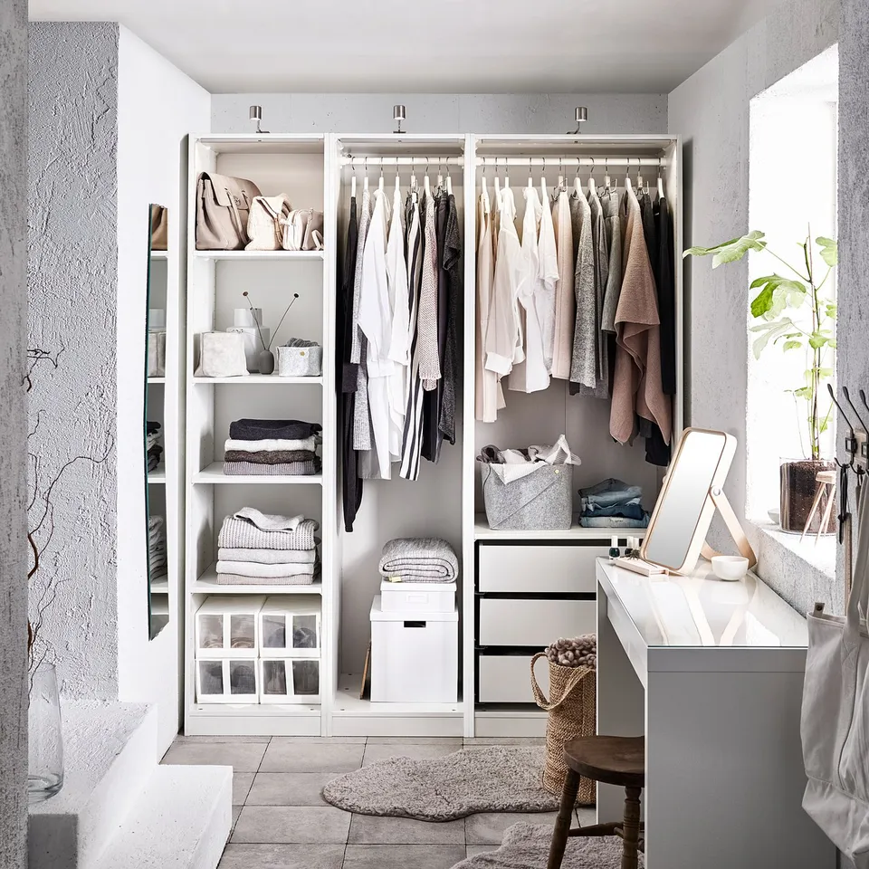 Modern white wardrobe with clothing, shelves, and drawers. A mirror and plant beside it.