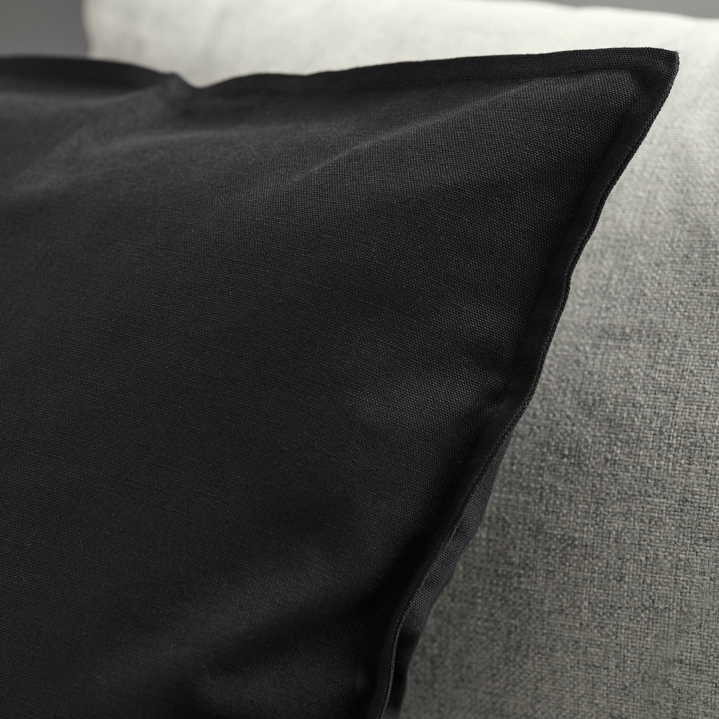 Black cushion cover on a grey surface, showing smooth texture and neat stitching.