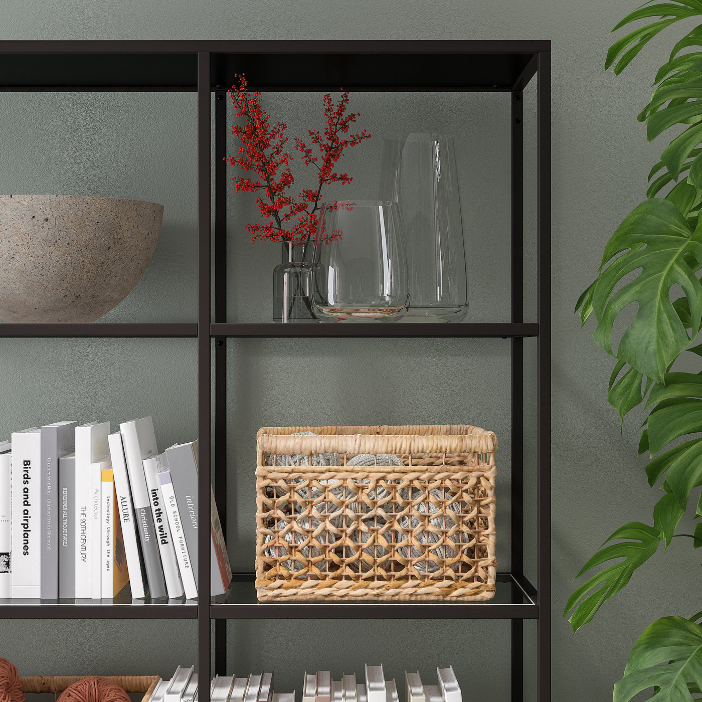 Black metal bookshelf with glass vases, red branches, woven basket, and books.