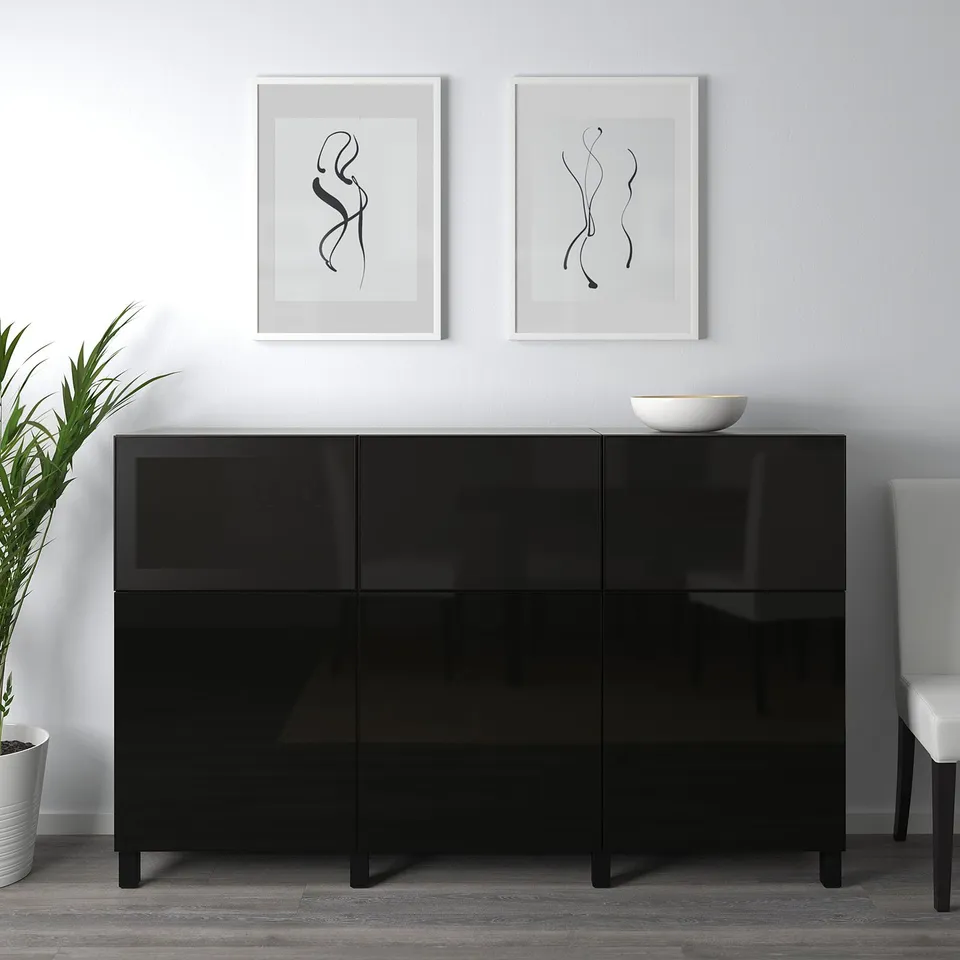 Black sideboard with glossy doors, placed against a white wall. Two framed artworks above it, one white bowl on top.